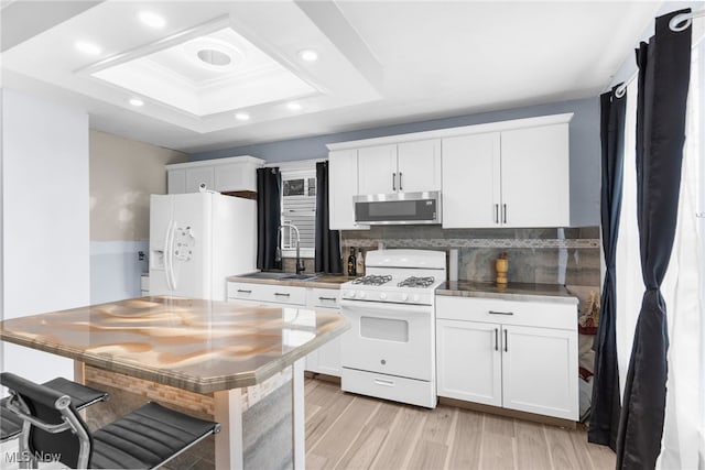 kitchen featuring white appliances, a sink, a tray ceiling, white cabinetry, and backsplash