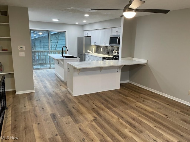 kitchen featuring stainless steel appliances, wood finished floors, a sink, white cabinetry, and light countertops