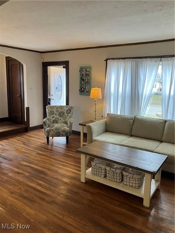 living room featuring arched walkways, crown molding, baseboards, and wood finished floors