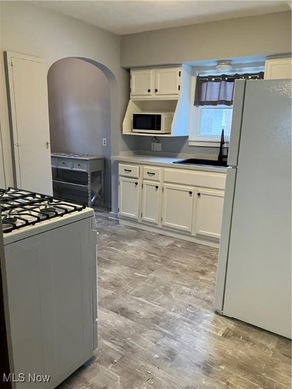 kitchen with white appliances, a sink, light wood-style flooring, and white cabinetry