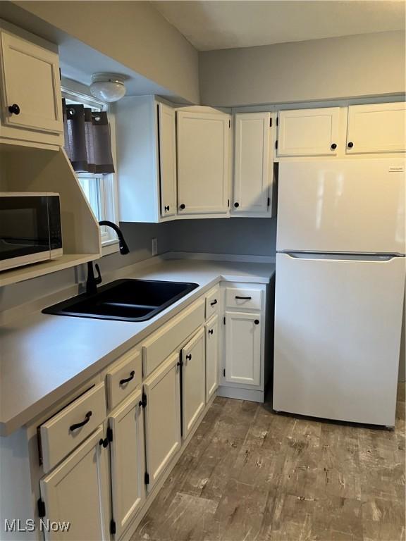 kitchen featuring white cabinets, wood finished floors, freestanding refrigerator, light countertops, and a sink