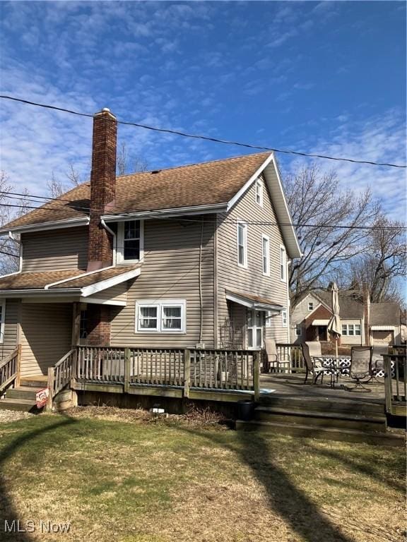 rear view of property with roof with shingles, a lawn, a chimney, and a wooden deck