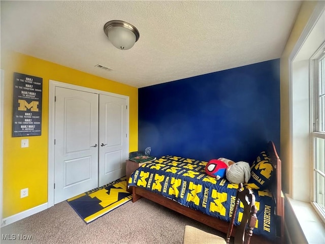 carpeted bedroom featuring a textured ceiling, a closet, visible vents, and baseboards