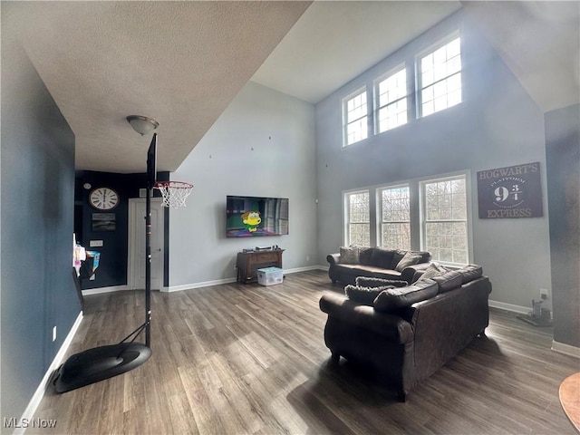 living area with a textured ceiling, wood finished floors, a towering ceiling, and baseboards