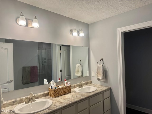 bathroom with a textured ceiling, double vanity, a stall shower, and a sink