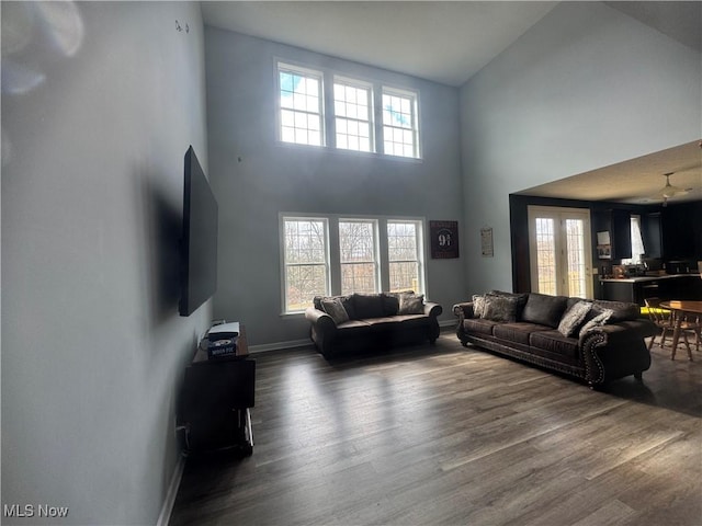 living room with dark wood finished floors, a towering ceiling, and baseboards