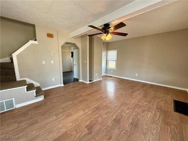 unfurnished living room with stairs, visible vents, arched walkways, and wood finished floors