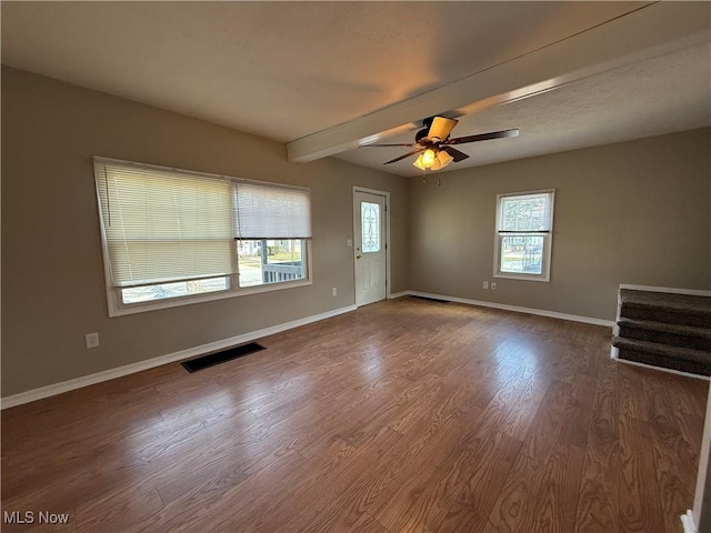 spare room with wood finished floors, a ceiling fan, visible vents, baseboards, and beam ceiling