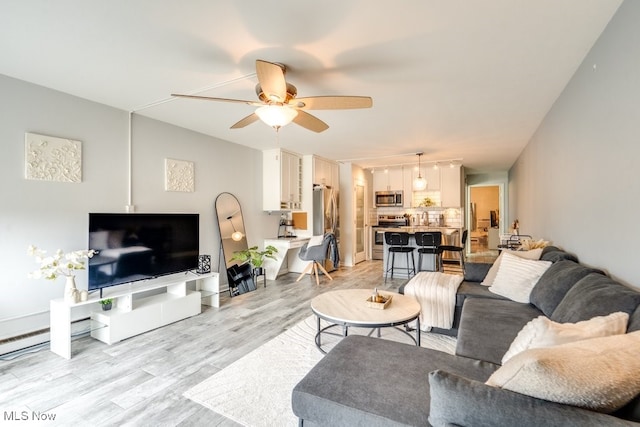 living room featuring light wood-type flooring, ceiling fan, and baseboards