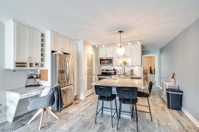 kitchen featuring light stone counters, stainless steel appliances, a sink, white cabinetry, and decorative backsplash