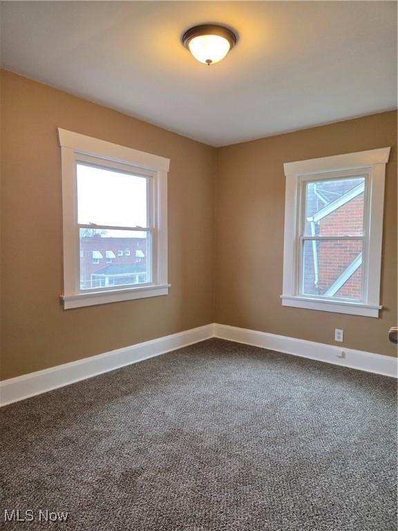 unfurnished room with dark carpet and baseboards