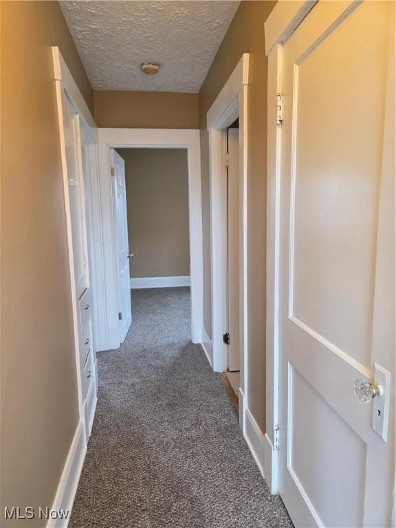 hallway featuring carpet, a textured ceiling, and baseboards