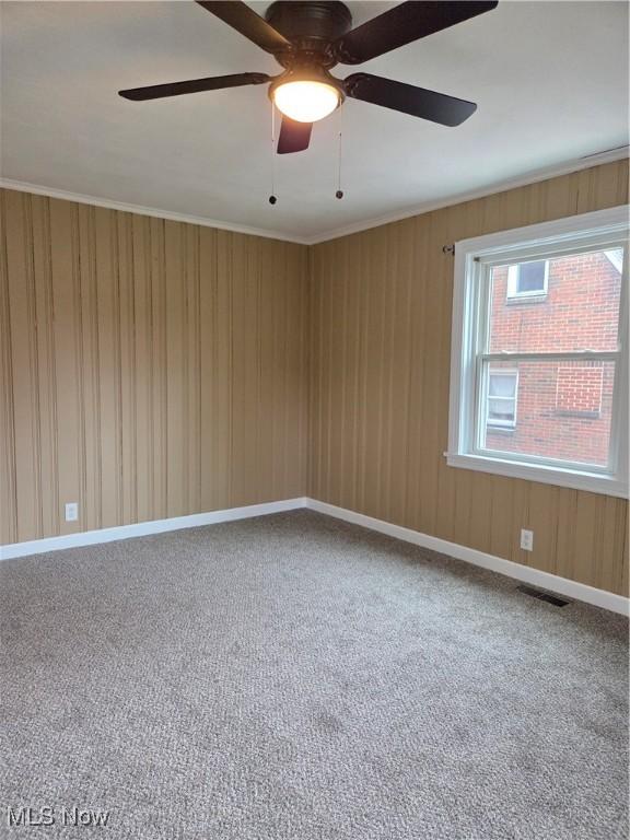 carpeted empty room featuring wooden walls, ornamental molding, visible vents, and baseboards