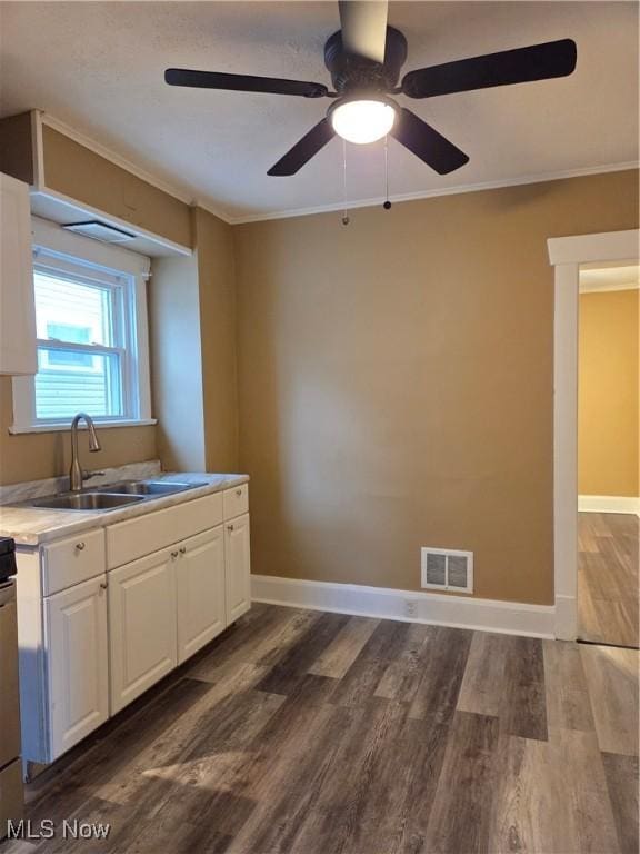 kitchen with visible vents, dark wood-style floors, ornamental molding, white cabinetry, and a sink