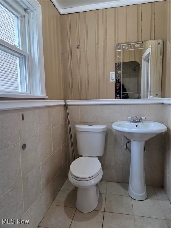 half bathroom with tile patterned flooring, tile walls, and toilet