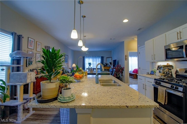 kitchen with light stone counters, decorative backsplash, appliances with stainless steel finishes, white cabinetry, and a sink