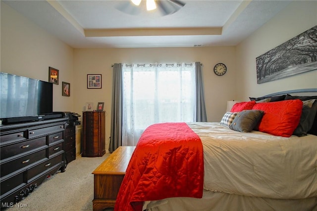 carpeted bedroom featuring ceiling fan and a raised ceiling