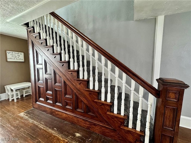 staircase featuring a textured ceiling, baseboards, and hardwood / wood-style flooring