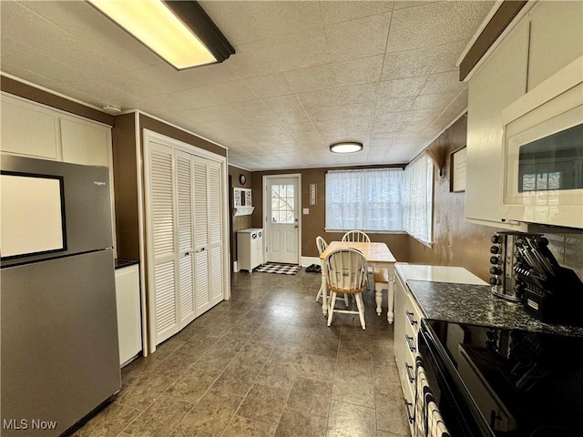 kitchen featuring white microwave, dark countertops, freestanding refrigerator, and white cabinetry