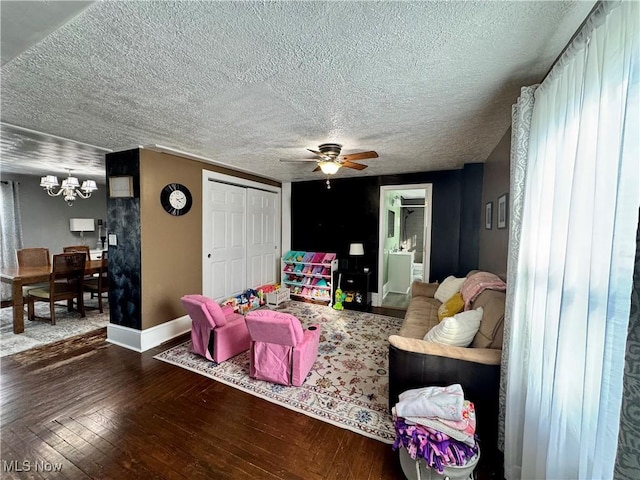 living room featuring a textured ceiling, dark wood-style flooring, ceiling fan with notable chandelier, and baseboards