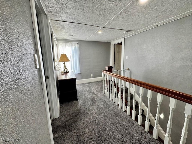 corridor featuring a textured ceiling, a textured wall, carpet floors, an upstairs landing, and baseboards