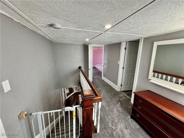 corridor with carpet floors, baseboards, a textured ceiling, and an upstairs landing