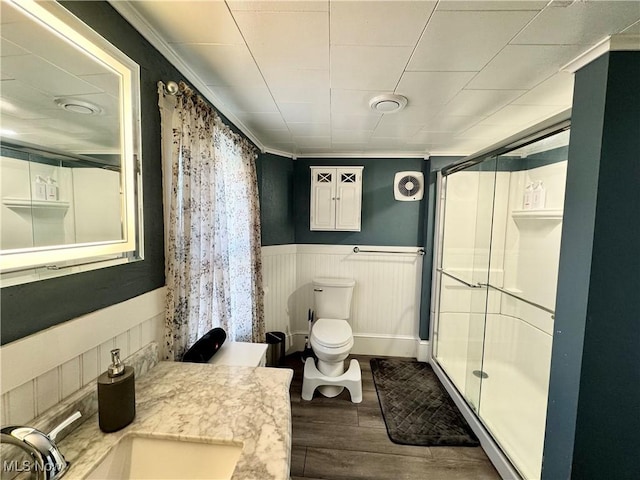 bathroom with wainscoting, toilet, wood finished floors, a shower stall, and a sink