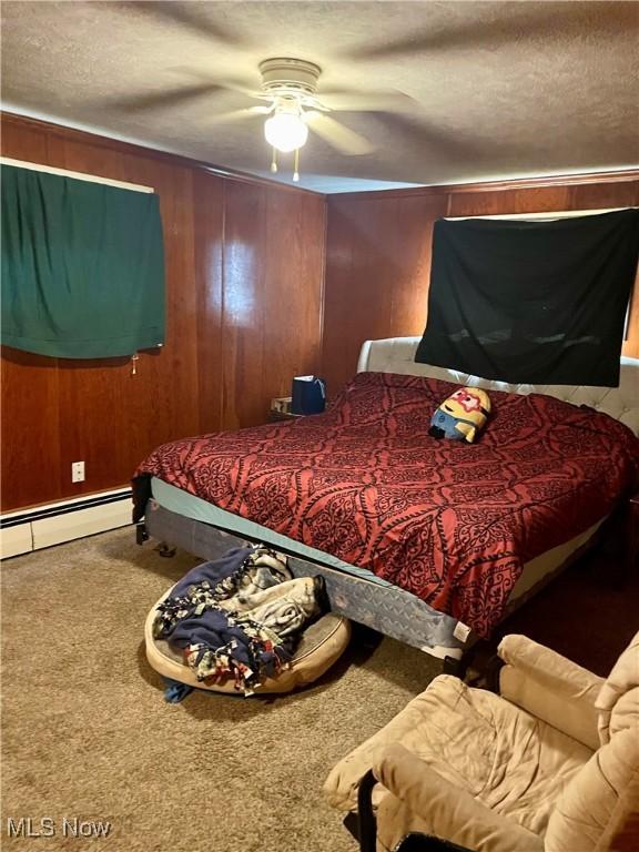 bedroom with carpet floors, wood walls, a baseboard heating unit, and a textured ceiling