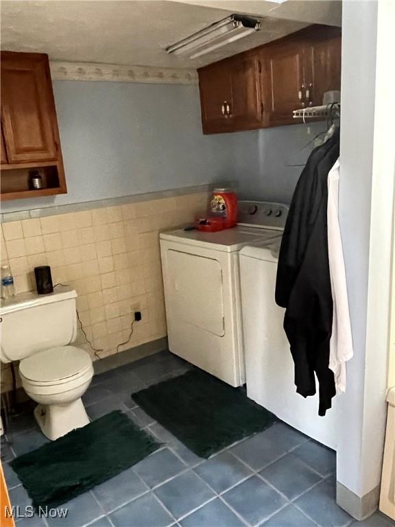 clothes washing area with laundry area, dark tile patterned floors, separate washer and dryer, and tile walls