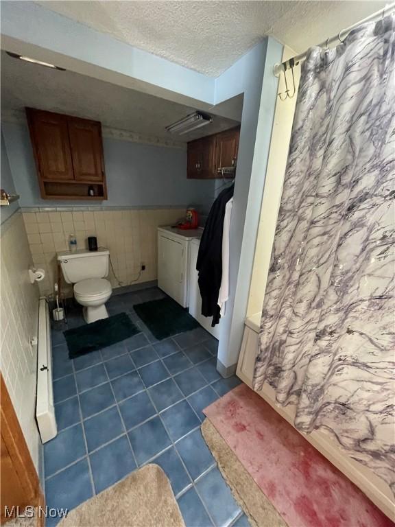 bathroom with wainscoting, toilet, tile patterned floors, curtained shower, and a textured ceiling