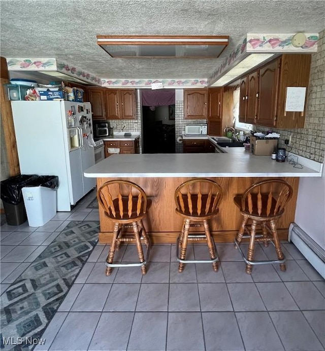 kitchen with white appliances, a kitchen breakfast bar, tile patterned floors, a peninsula, and a sink