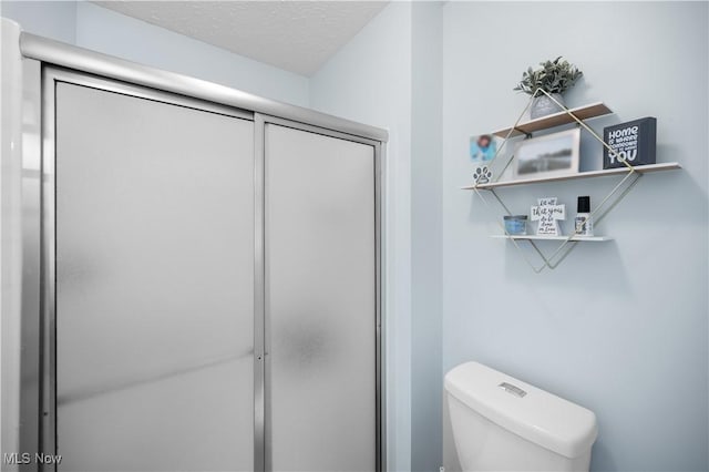 bathroom with toilet, a textured ceiling, and a shower stall