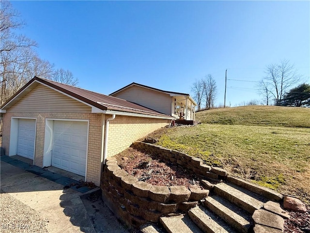 view of home's exterior with an attached garage, metal roof, a lawn, and brick siding