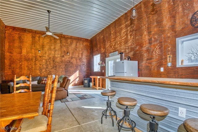 interior space featuring concrete flooring, ceiling fan, a dry bar, and freestanding refrigerator