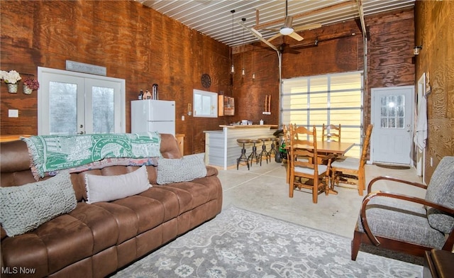 living room with french doors, concrete floors, a ceiling fan, and wooden walls