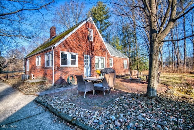 view of property exterior with brick siding, a chimney, central air condition unit, a patio area, and fence