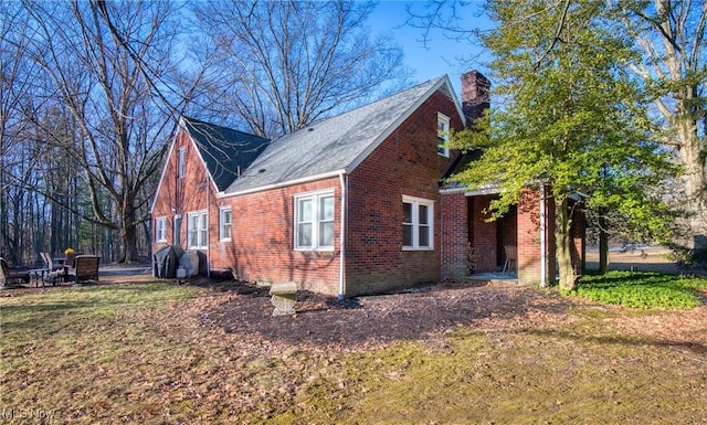 view of side of property featuring a chimney, a lawn, and brick siding