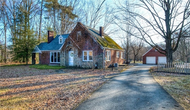 view of front of home featuring an outbuilding, brick siding, a detached garage, a chimney, and fence