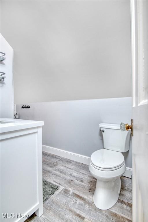 half bathroom featuring toilet, baseboards, wood finished floors, and vanity