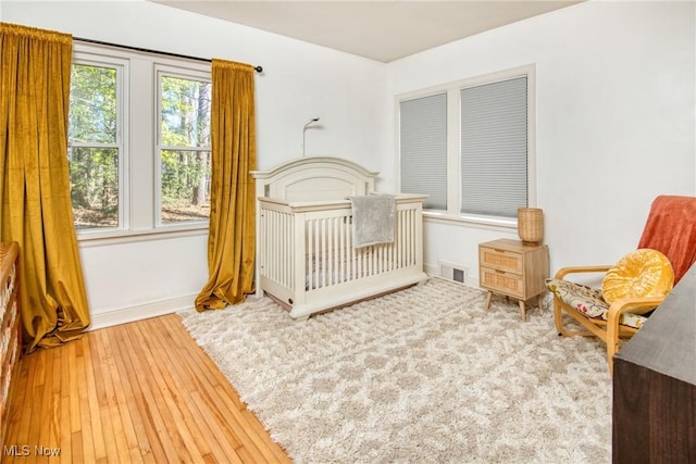 bedroom featuring wood-type flooring, visible vents, a crib, and baseboards