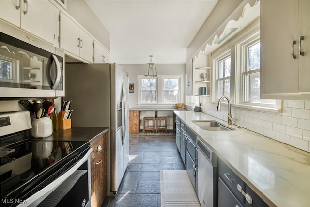 kitchen featuring stainless steel appliances, a sink, white cabinets, backsplash, and stone tile flooring