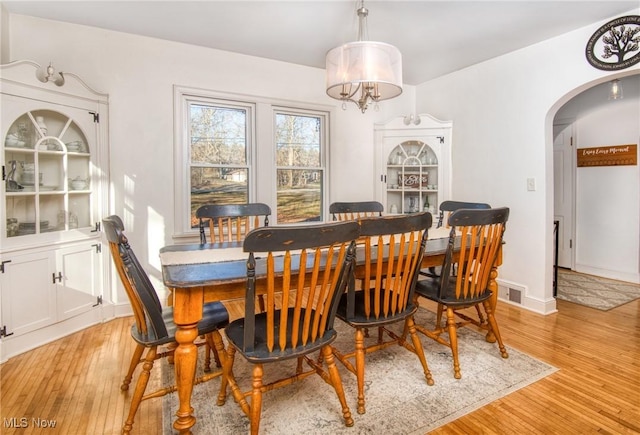 dining space with light wood finished floors, visible vents, arched walkways, and baseboards