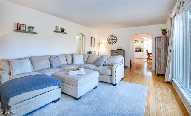 living area with arched walkways, a wealth of natural light, and light wood-style flooring