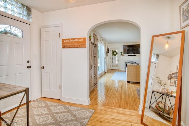 entryway featuring arched walkways, a fireplace, light wood-style flooring, and baseboards