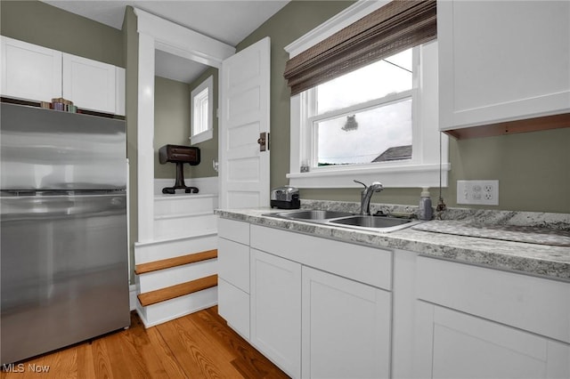 kitchen featuring light stone counters, freestanding refrigerator, light wood-type flooring, white cabinetry, and a sink