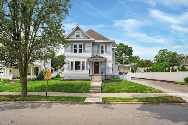 view of front facade featuring concrete driveway, fence, and a front lawn