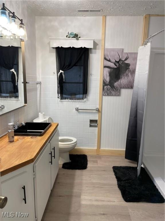 full bath with toilet, wood finished floors, vanity, tile walls, and a shower with curtain