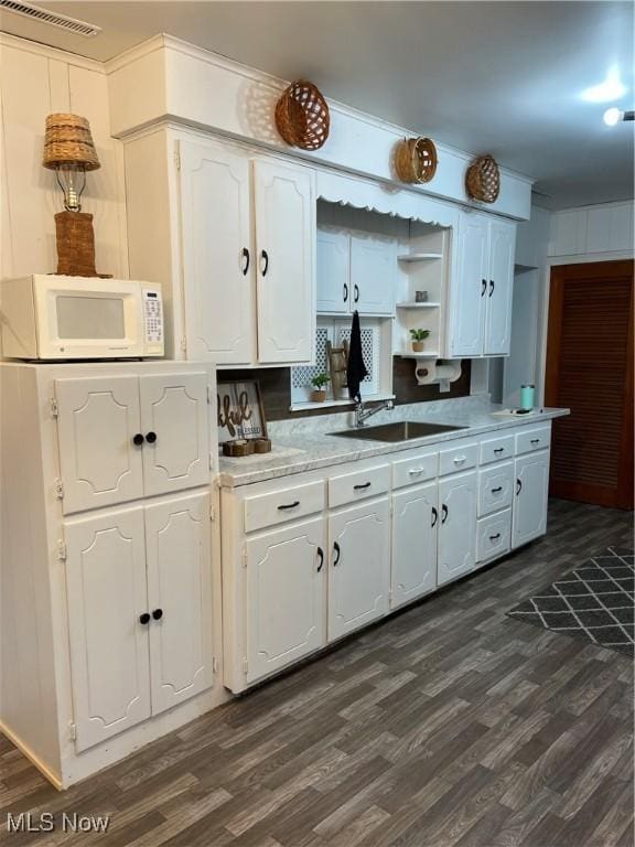 kitchen featuring open shelves, visible vents, white microwave, white cabinets, and a sink