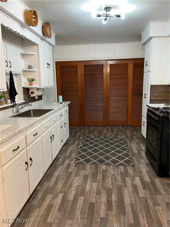 kitchen featuring dark wood finished floors, black gas range oven, light countertops, white cabinetry, and a sink