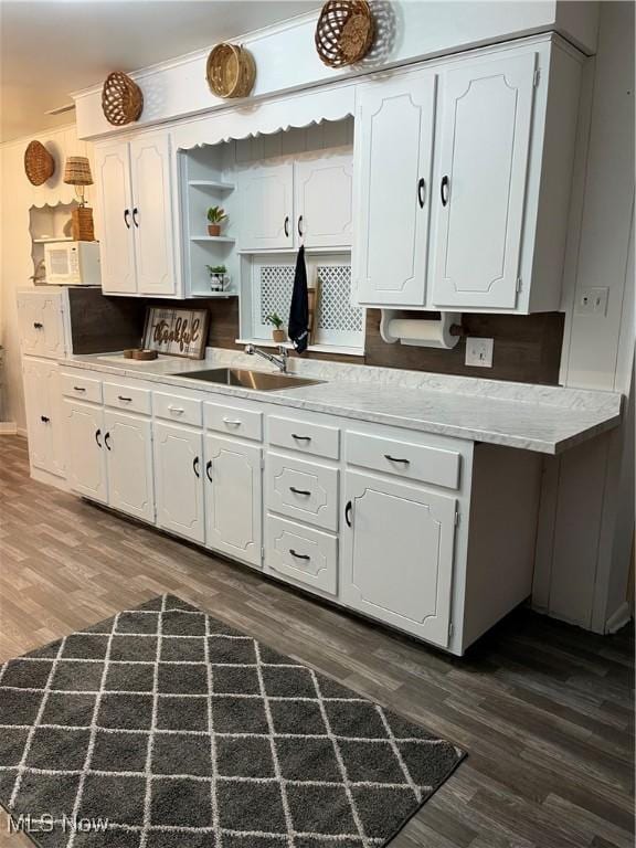 kitchen featuring white microwave, white cabinetry, dark wood-style flooring, and a sink